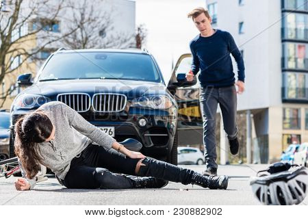 Full length of a young female bicyclist fallen down on street with serious injuries after traffic accident with the 4x4 car of a young man