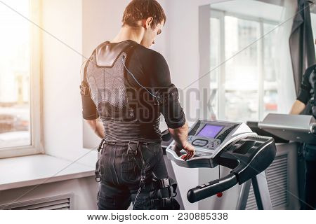 Ems Training. Fit Man Wearing Black Electromiostimulation Suit Preparing For Running On Treadmill Ne
