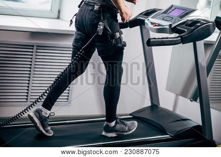 Close Up Of Legs Of Man Wearing Black Electromiostimulation Suit Running On Treadmill Near Window