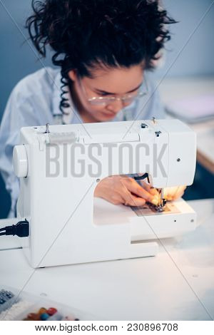 Young Woman With Dark Curly Hair Sewing On Sewing Machine In Room. Small Business. Designing Clother