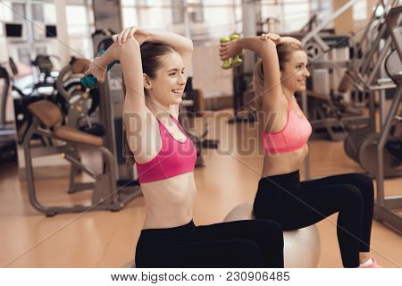 Two Women In Sportswear Sitting Doing Exercises With Dumbbells At The Gym. They Look Happy, Fashiona