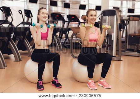 Mother And Daughter In Sportswear Sitting Doing Exercises With Dumbbells At The Gym. They Look Happy