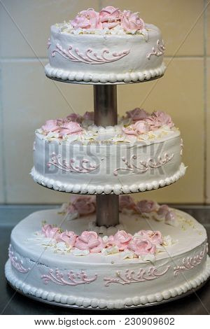 Three-tiered Wedding Cake Is Decorated With Flowers And Stands On The Table Next To A Plate And Cutl