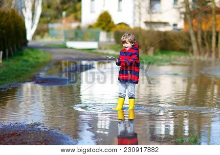 Little Kid Boy Wearing Yellow Rain Boots And Walking And Jumping Into Puddle On Warm Sunny Spring Da