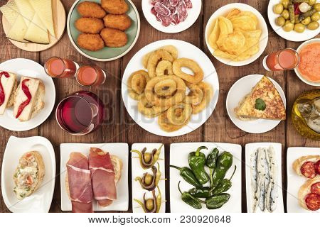 The Food Of Spain. An Overhead Photo Of Many Different Spanish Tapas, Shot From Above On A Dark Rust
