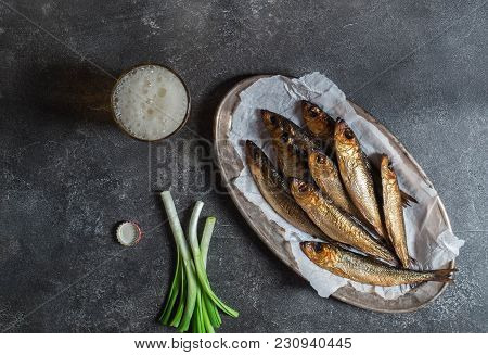 A Few Smoked Baltic Herring On A Metal Oval Dish And Beer In Glass On A Dark Background. Top View