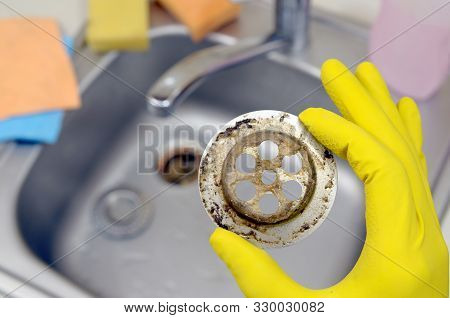 Cleaner In Rubber Gloves Shows Waste In The Plughole Protector Of A Kitchen Sink