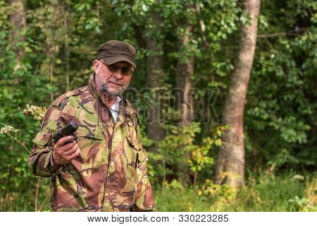An Old Bearded Bandit With A Gun In His Hand. Russian Gangster In Camouflage Military Uniform. The C
