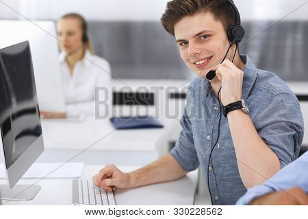 Call Center. Group Of Casual Dressed Operators At Work. Focus On Young Businessman In Headset At Cus