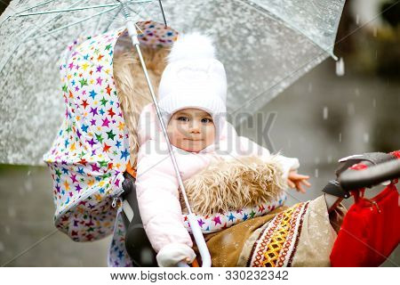 Cute Little Beautiful Baby Girl Sitting In The Pram Or Stroller On Cold Day With Sleet, Rain And Sno