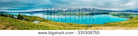 Panoramic picture of  incredibly blue lake Tekapo with overcast sky seen from Mt. John observatory. Canterbury region, New Zealand