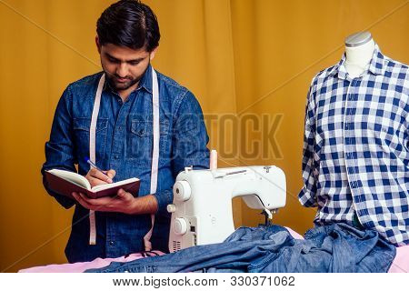 Handsome Indian Tailor Man In A Stylish Shirt Working With Dreen Jeans Cotton Textile At Home Worksh