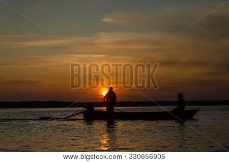 The Fishermen And Boat Silhouette On The Lake In Sunrise.