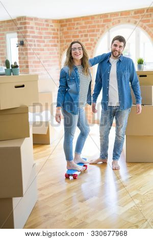 Young couple moving to a new home, having fun riding a skateboar
