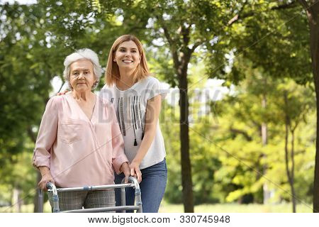 Caretaker Helping Elderly Woman With Walking Frame Outdoors