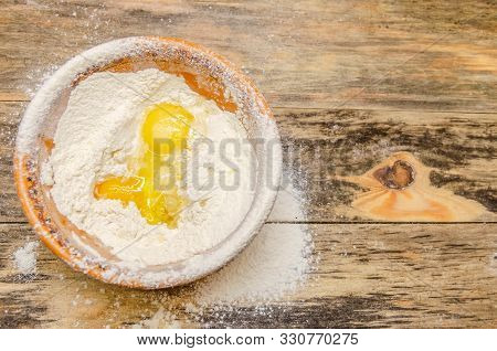Brown Bowl Of Flour And Egg Stands On A Wooden Background, Top View, Copy Space