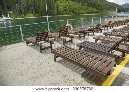 Row Of Empty Wooden Beach Chairs Near Water.