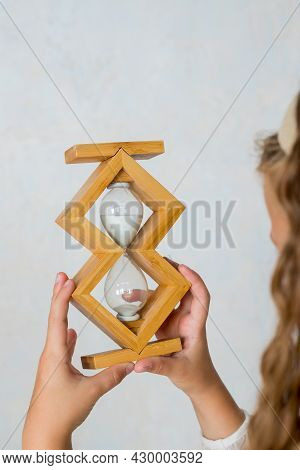 Schoolgirl Is Holding Sandglass In Classroom. Small Girl In Time Management Concept. Education And S