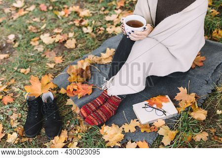 Woman Had A Picnic In Autumn Forest. Girl In Jeans, Wjite Scarf And Red Knitted Socks Sitting On Pla