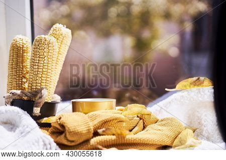 Corns, Autumn Leaves, Pine Cones And Coffee Cup On Windowsill. Creative Autumnal Background Near The
