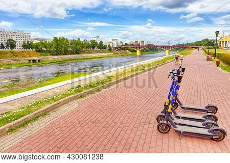 Vitebsk, Belarus- 1 August, 2021: Line Of Electric Scooters In Front Of Dvina River And Bridge In Vi