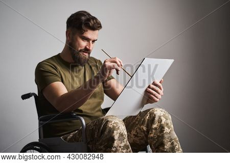 Ex-serviceman Sitting In A Wheelchair And Painting A Picture On A Canvas