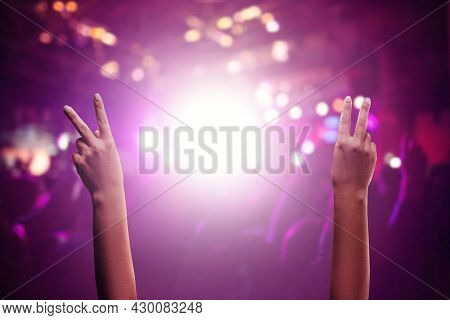 Enjoying Show Or Concert. Raised Hands Demonstrate V-sign At Crowded Hall During Live Music Concert