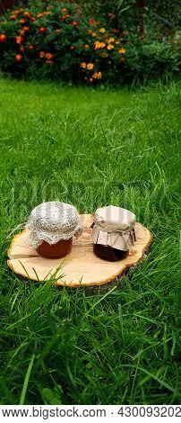 Small Jars Of Honey Of Different Varieties And A Honey Dipper On A Stand Made Of Cut Wood.