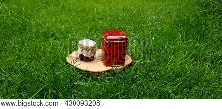 A Jar Of Honey And A Metal Box Of Tea On A Wooden Cut In The Grass