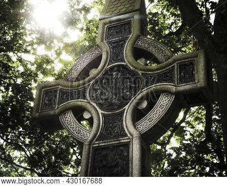 Celtic Cross Backlit With A Background Of Trees.