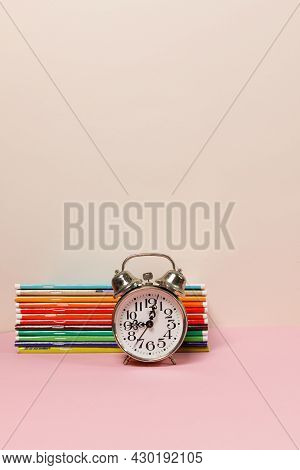 A Stack Of Colorful Notebooks And An Alarm Clock On The Table. A Vertical Frame With Space. Pastel C