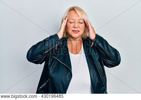 Middle age blonde woman wearing leather jacket with hand on head for pain in head because stress. suffering migraine. 