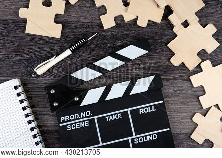Cinematic  Clapper With Notepad, Pen And Puzzle Pieces On A Table Top View