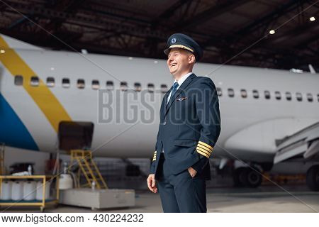 Portrait Of Happy Pilot In Uniform Looking Away, Ready For Flight, Standing In Front Of Big Passenge