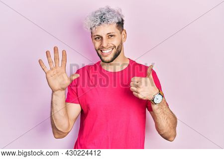 Young hispanic man with modern dyed hair wearing casual pink t shirt showing and pointing up with fingers number six while smiling confident and happy. 