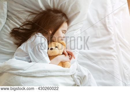 Baby Lying In Bed With Taddy Bear. Little Girl Sleeps With Knitted Toy
