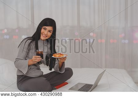 Asian Women Eat Pizza And Cola Drink For Dinner Before Going To Bed, Eating Happily In Bed In The Ho