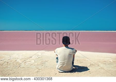 Back View Of Unrecognizable Man, Wearing Gray Tshirt And Baseball Cap, Sitting Against Pink Lanke An