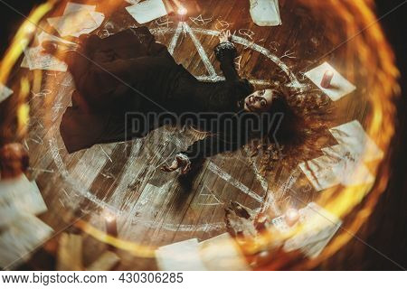 A portrait of a scary witch lying on the floor in the ring of fire in the wooden house. Magic, dark force, spell. Halloween.