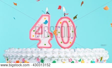 Colorful tasty birthday cake with candles shaped like the number 40. Pastel blue background.