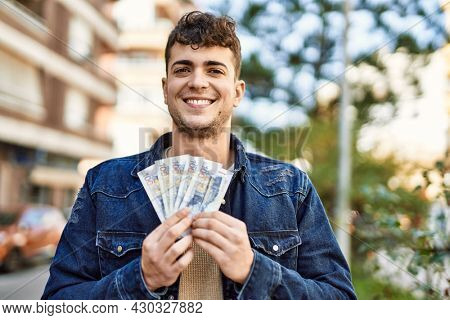 Young hispanic man smiling happy holding peruvian sol banknotes at the city