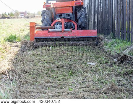 A Tractor With A Mower Attached Mulches Dry Grass Along The Fence. Land Plot Processing