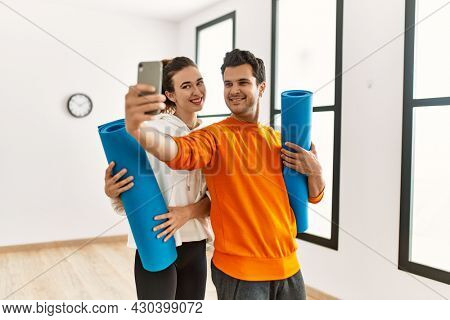 Young hispanic sporty couple holding yoga mat and making selfie by the smartphone at sport center.