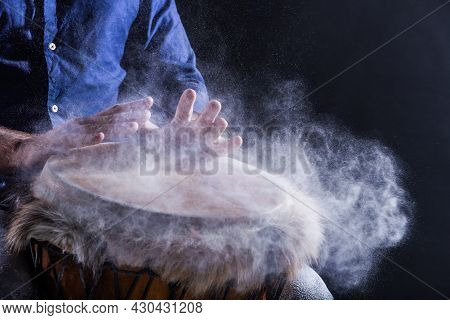 Man Is Playing On Djembe Drum, Covered With Talcum Powder. Flour Splashes On Dark Background. Summer