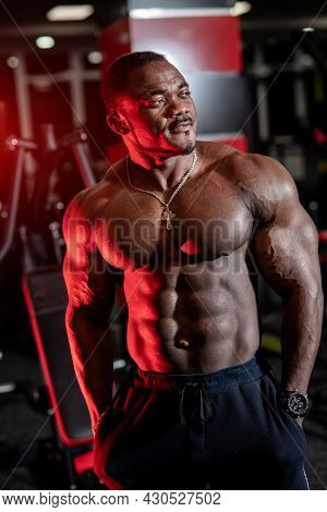 Strong Halfnaked African American Bodybuilder Standing In Contemporary Gym And Looking Away.