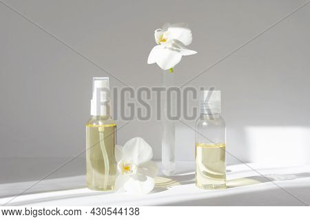 Mock-up Of Two Glass Bottles With Spray Gun And Test Tube With Orchid Flowers On White Background In