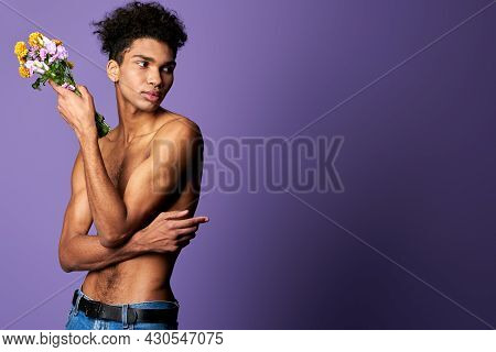 Portrait Of Latino Transgender Male Model With Bouquet On Purple Background. Young Man Nacked Torso