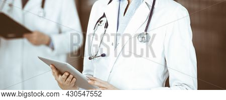 Unknown Woman Doctor Iusing Tablet Computer In Her Hands, While Standing In Clinic. Medicine Concept