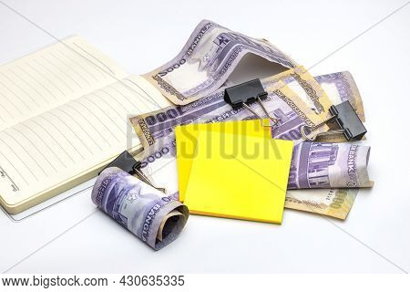 Scattered Thousand Taka Bangladesh Banknotes With A Notebook, Black Binder, And Sticky Notes On Whit