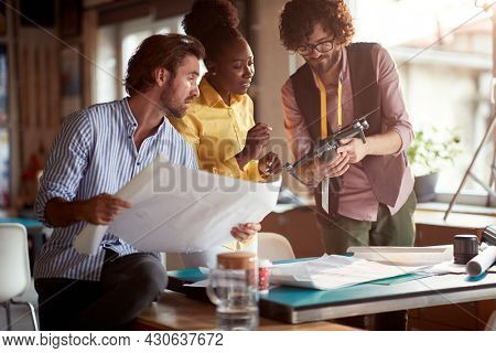 young beardy caucasian guy presenting drone as a solution for filming an advertisement to his male boss and afro-american female colleague